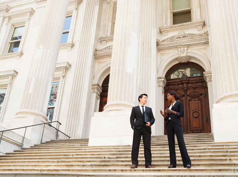 Two people dressed in business suits talk on a set of steps outside a courthouse