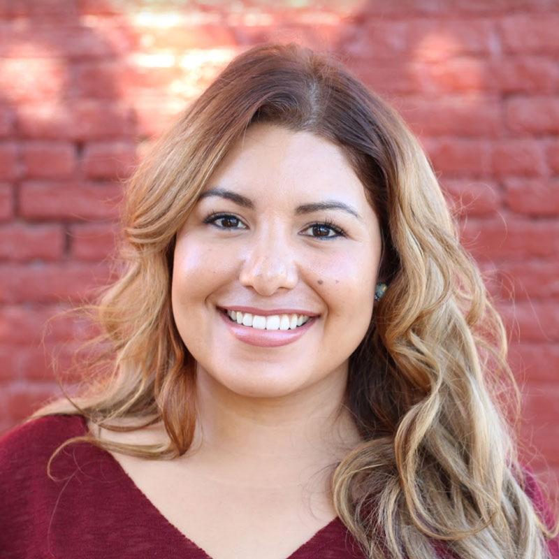 Woman's face smiling with red brick in background