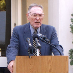 This is an image of a man standing a a lectern addressing an audience at an event.