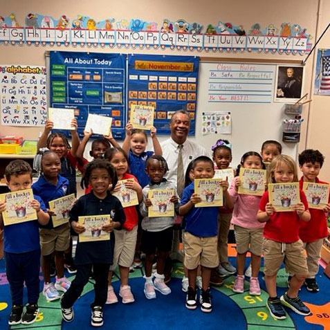 Judge Williams sits behind a group of students in a classroom holding a book.