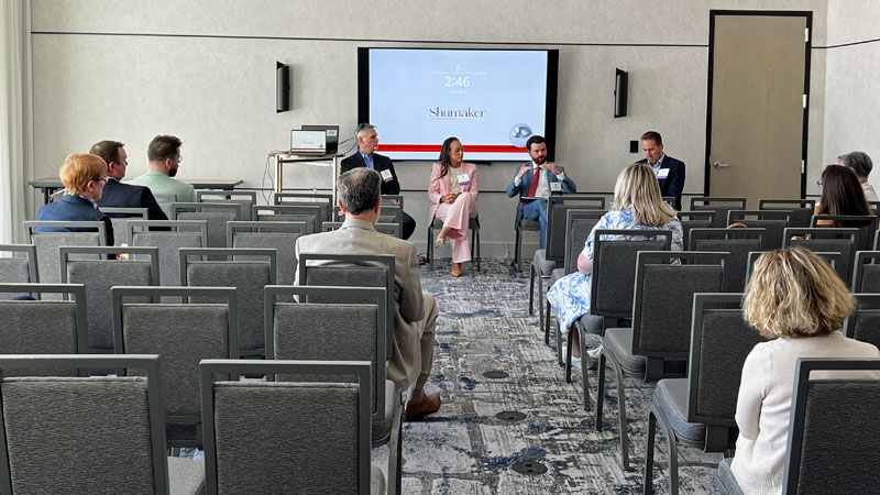 One moderator and three people sit in the front of a room and speak to an audience.