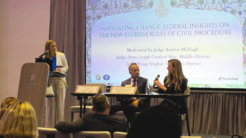 One moderator and two people sit on an elevated platform while they speak to people in an audience.