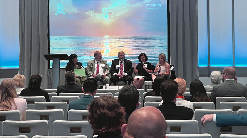 One moderator and four people sit on an elevated platform and speak to an audience.