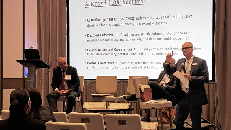 One moderator and two people sit on an elevated platform and speak to an audience.